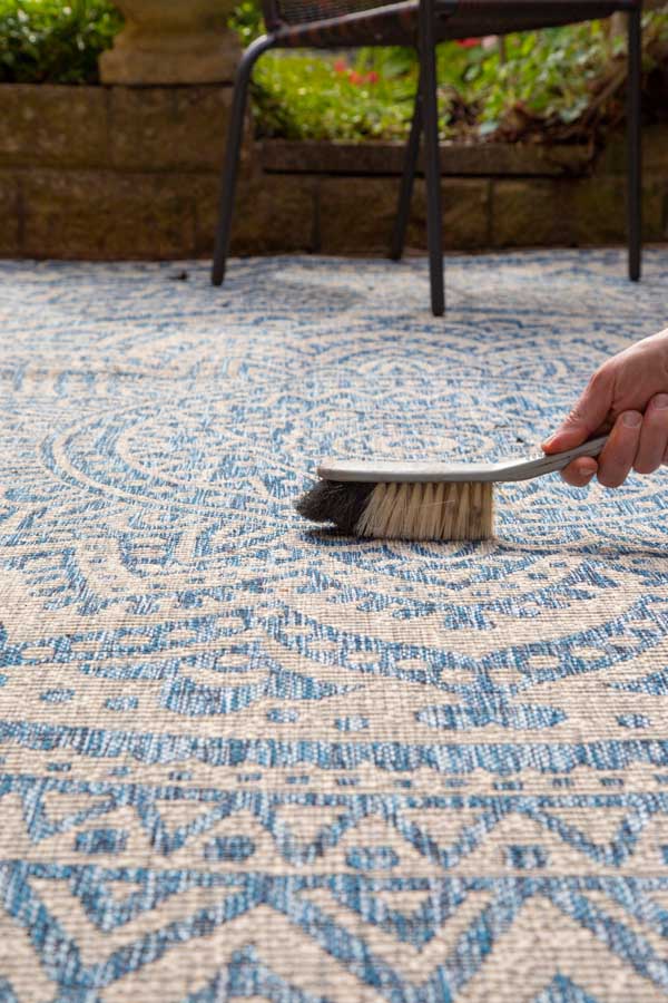 Person using a small brush to dust off an outdoor rug