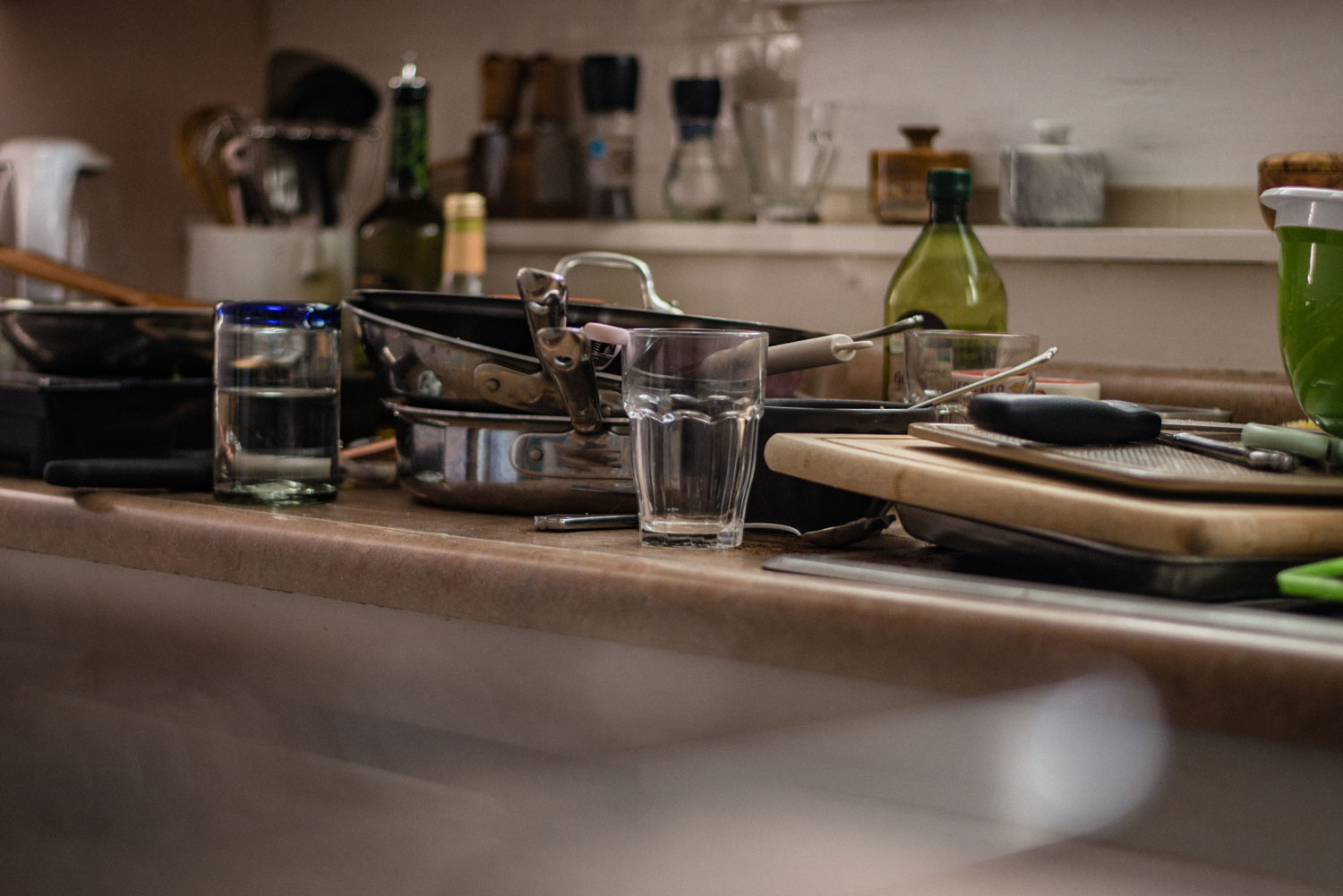 A messy counter and sink is filled to the brim with dirty dishes and cluttered with bowls, pans, and utensils that need washing.
