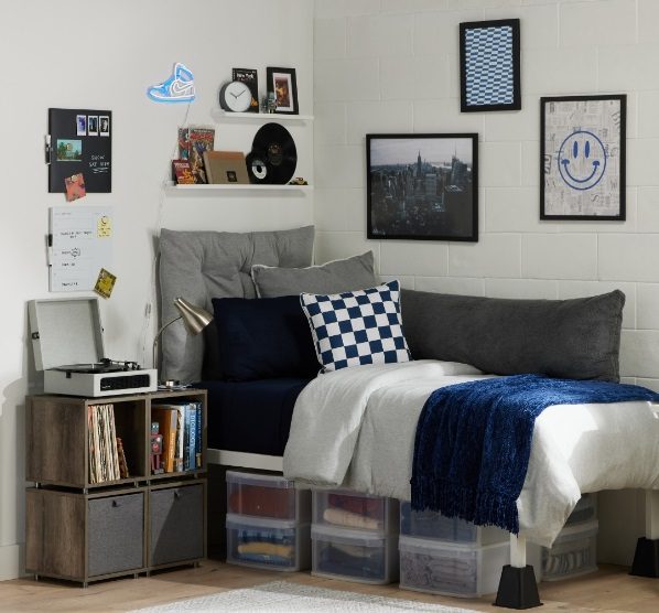 Image of a decorated dorm room with a bed lifted by bed risers and storage bins tucked underneath