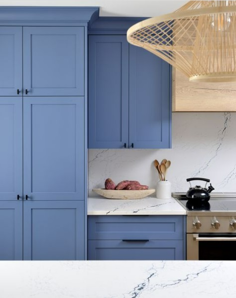 An updated kitchen with bright blue cabinets and marbled countertops and backsplash