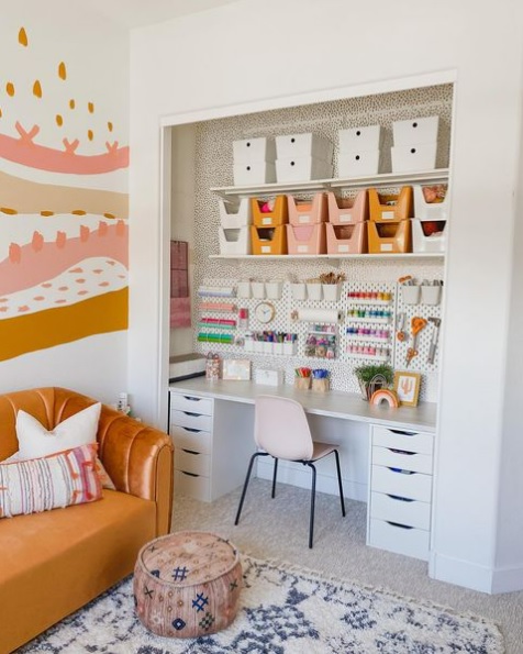 A closet turned craft space with a desk, peg board, and shelves full of bins.
