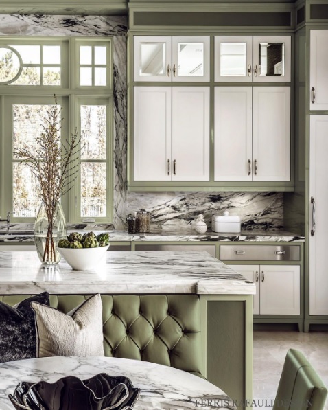 A renovated kitchen with marble countertops and backsplash, white cabinets, and moss green accents