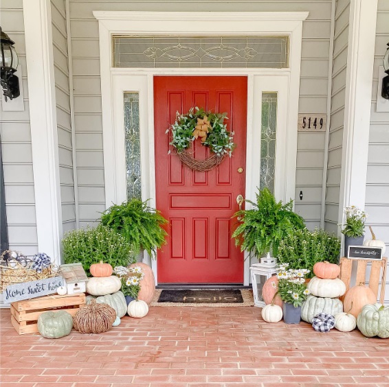 Front door with potted plants, pumpkins, and crates on either side