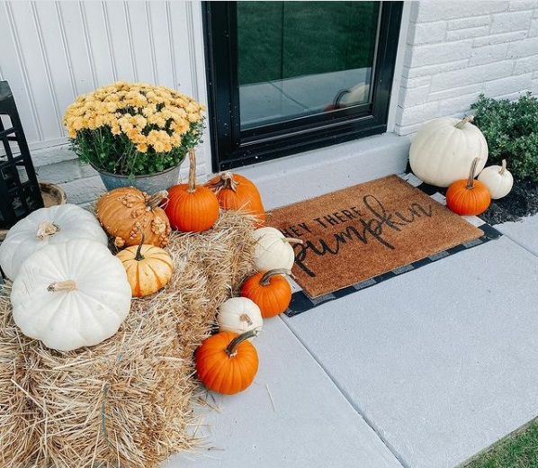 Hay bales set in front of a door with pumpkins stacked on and around them 