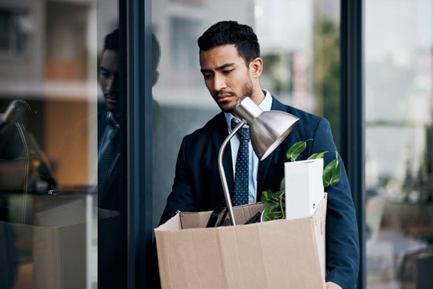 Man looking upset while holding a box filled with office belongings