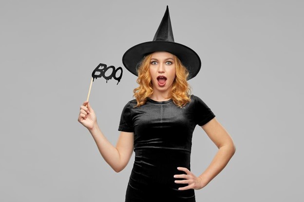 Surprised lady in a witch costume holding a "Boo" sign on a stick