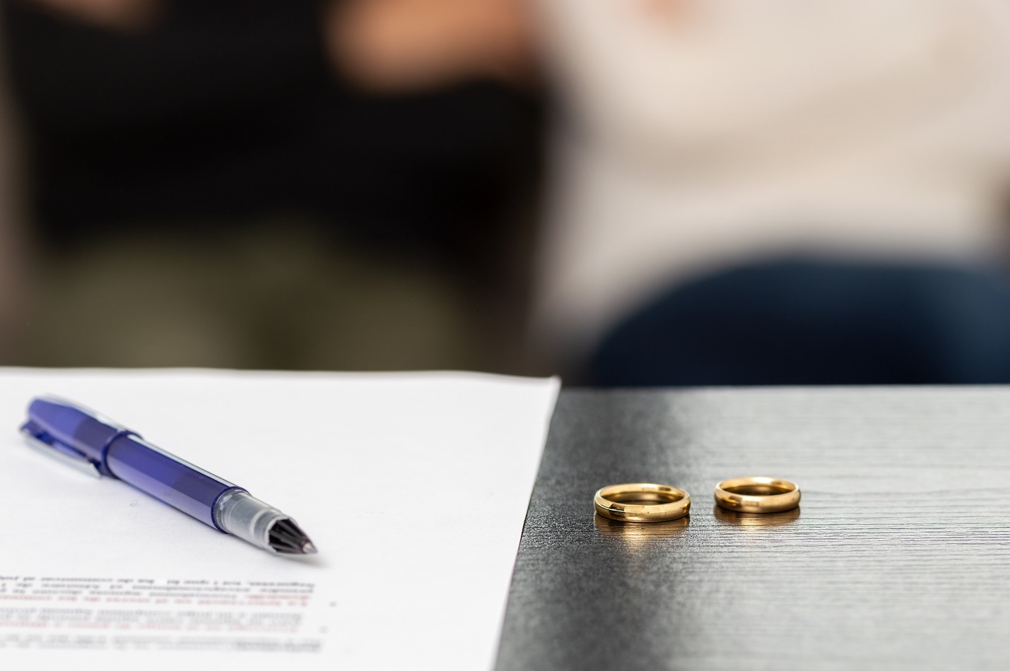 Two wedding bands on a table next to divorce papers and a pen