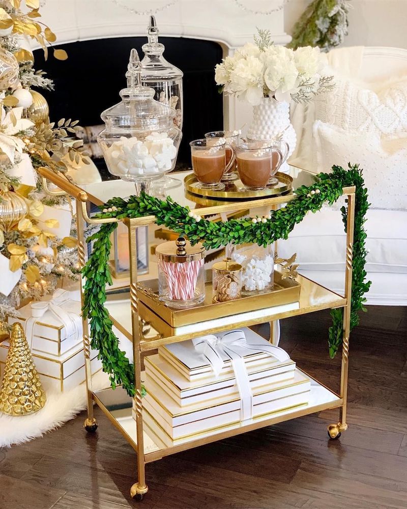 Bar cart decked out with glass mugs of hot cocoa and candy toppings.