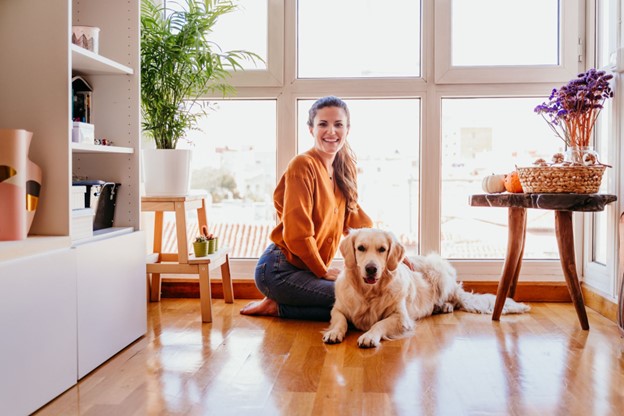 Smiling woman sitting on the floor of her home with her golden retriever dog