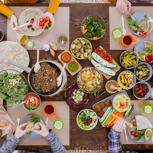Bird's eye view of a table set with a variety of meatless dishes as people serve themselves.
