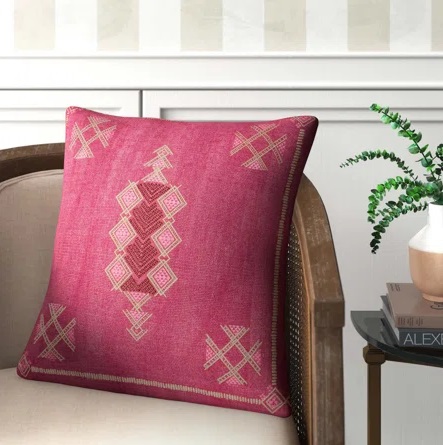 Magenta embroidered throw pillow set on a neutral armchair.