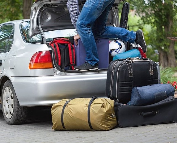 person struggling to pack belongings into full car trunk