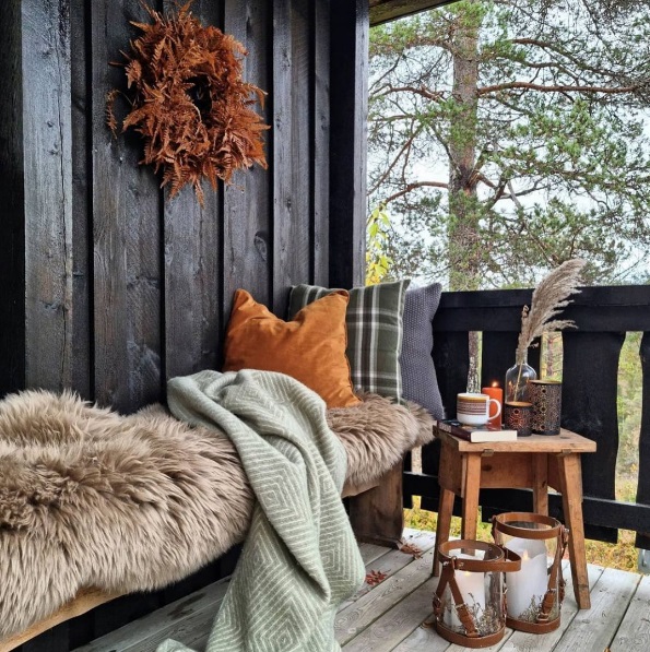 Porch with a small table and bench that's decorated with throw blankets and pillows