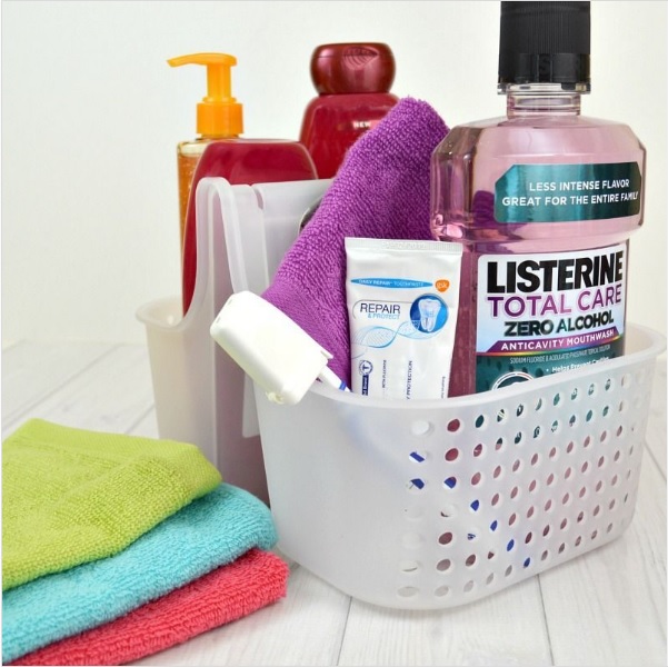 A shower caddy filled with shower and oral care supplies sitting next to a stack of washcloths