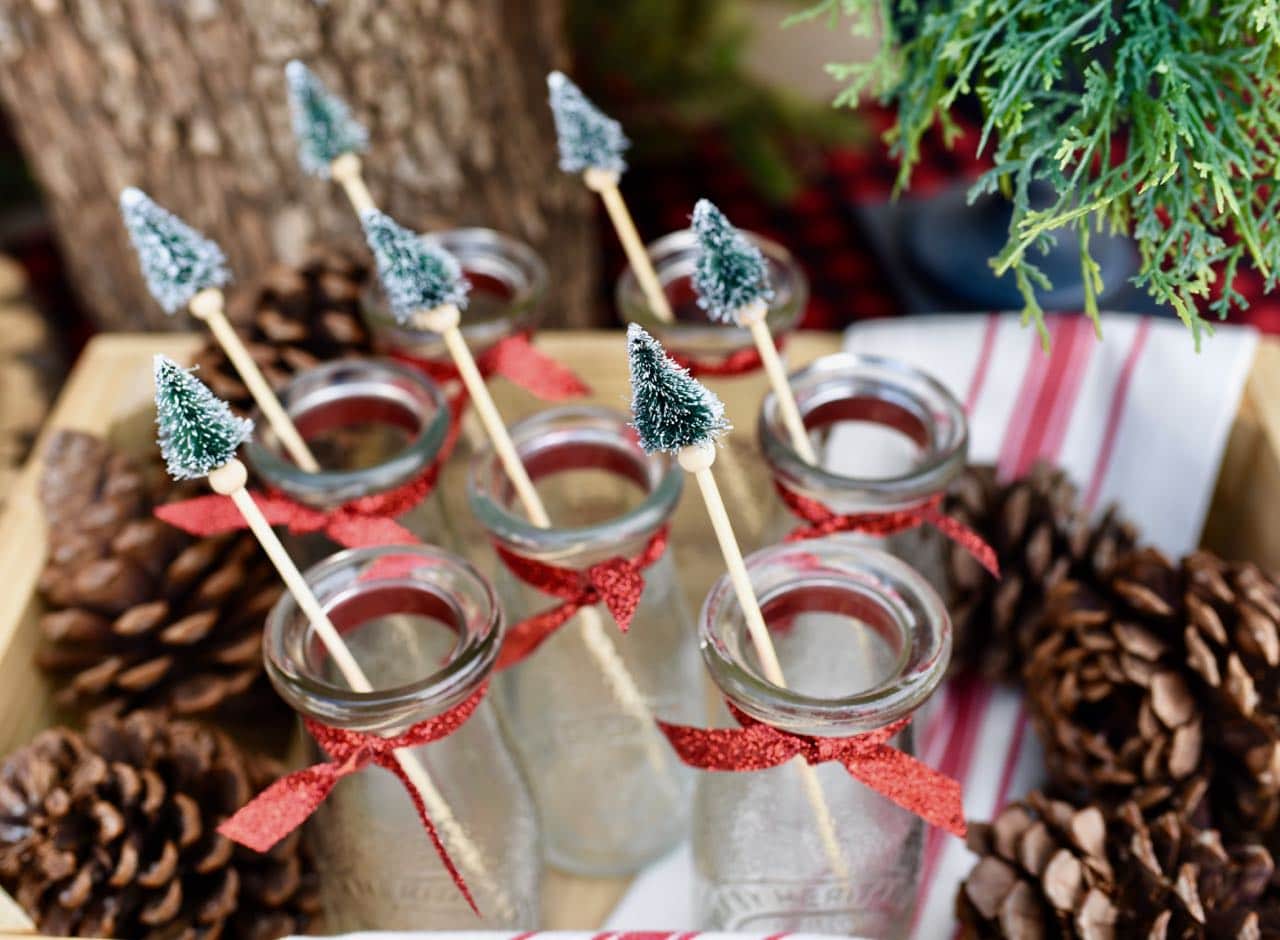Glasses with a red ribbon around the neck and bottle brush swizzle sticks sticking out of the top.
