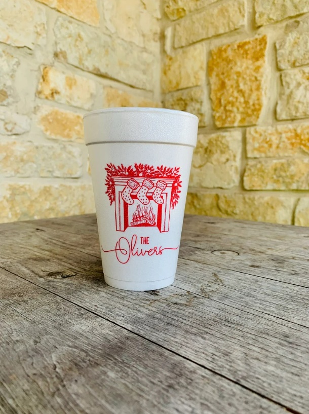 A white plastic cup with a fireplace mantle design and The Olivers printed in red on the front.
