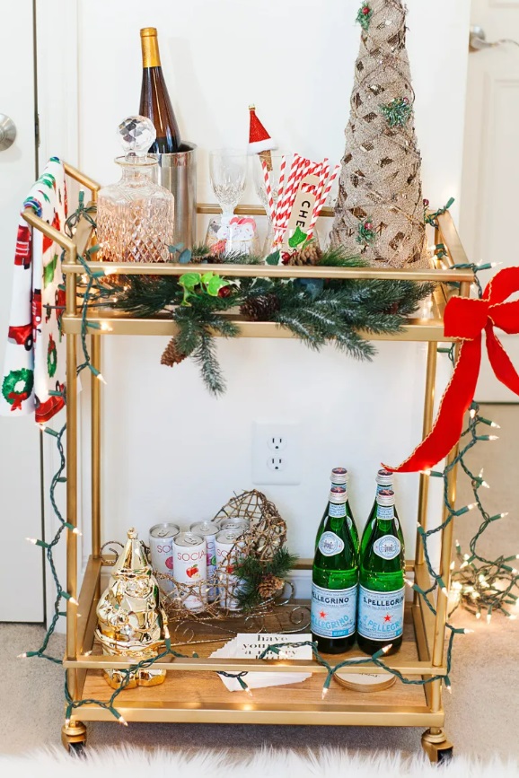 A festive bar cart with string lights, pine boughs, and a bow.
