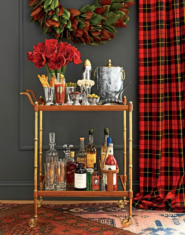Bar cart with a vase of red flowers, drink toppers, and and ice bucket on the top and drink bottles and glasses on the bottom.