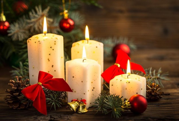 four lit candles surrounded by bows and holiday decorations