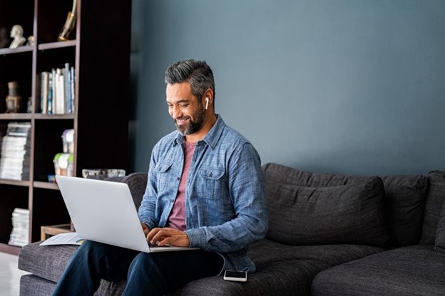 Smiling man sitting on a couch while working on a laptop