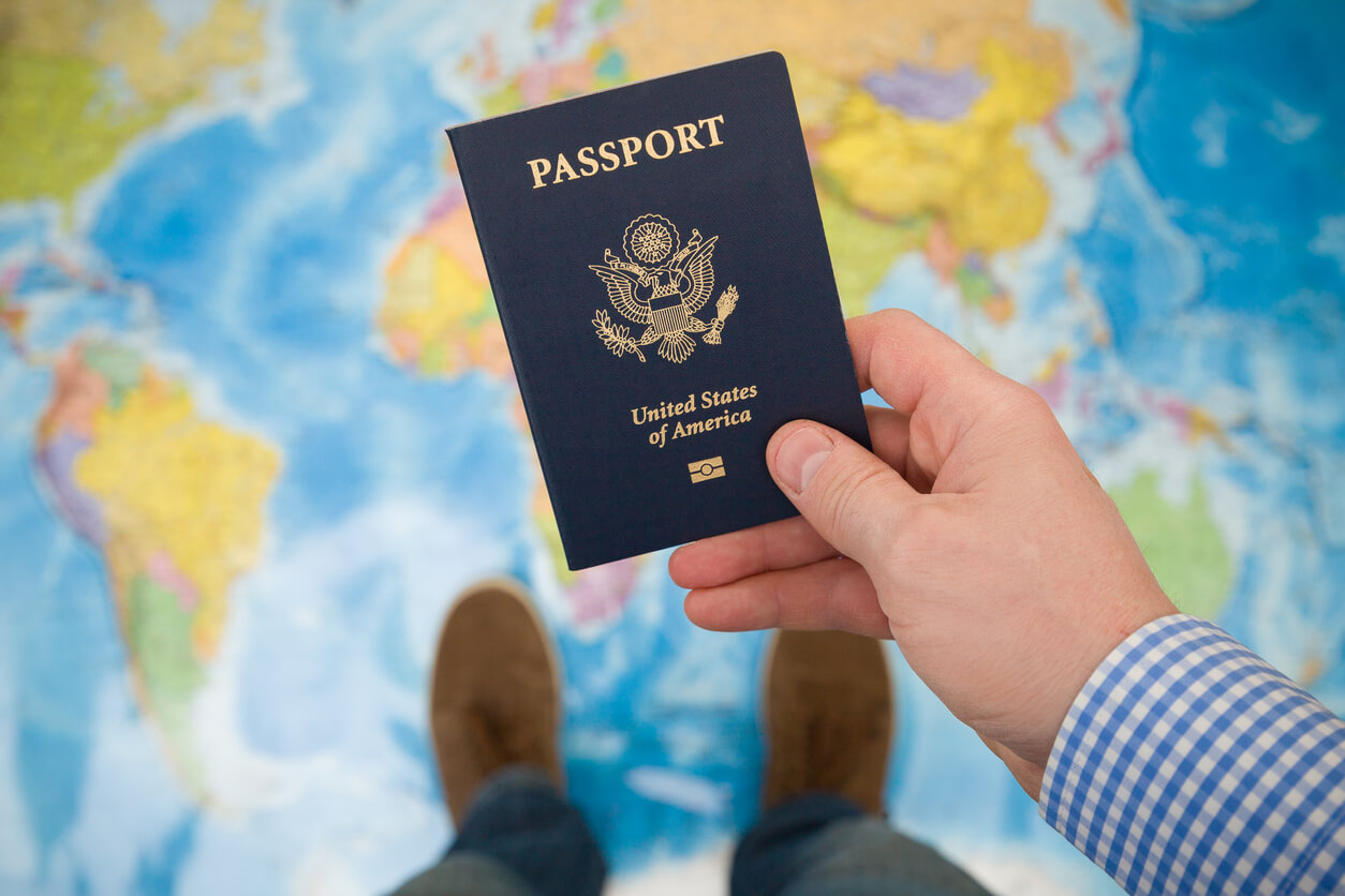 A person holding a passport in their hand. In the background, a map of the world is visible.