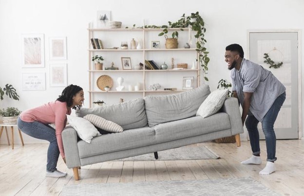 a young couple is picking up a gray couch to move it