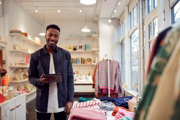 the owner of a small boutique is holding a point-of-sale device and smiling