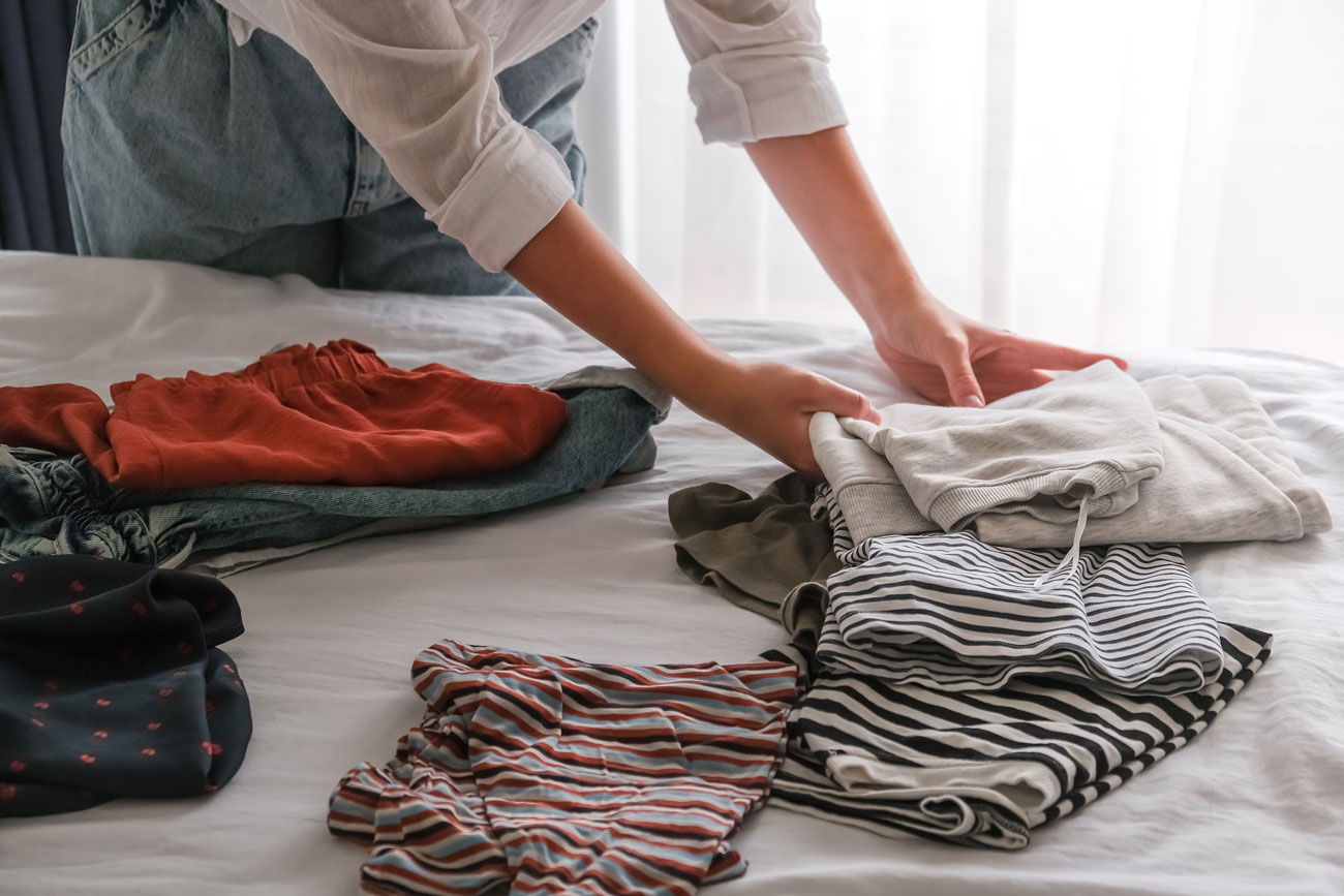 Person sorting clothes on a bed in order to organize their closet