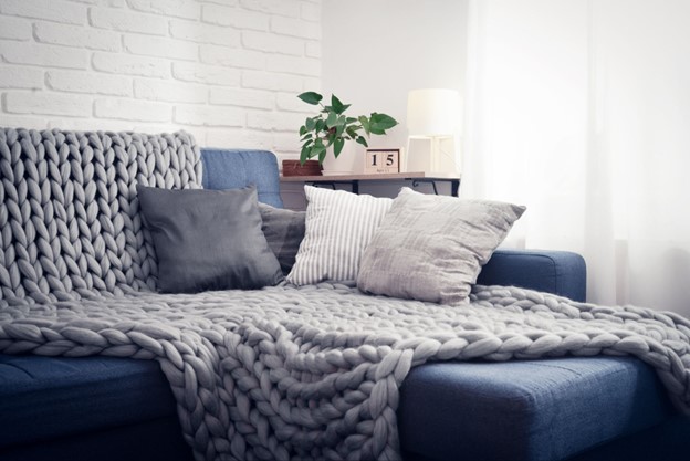 A chunky knit blanket draped across a couch with throw pillows piled on top