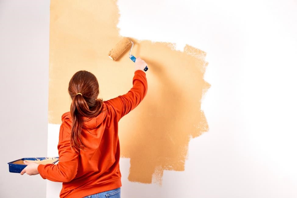 A woman in an orange sweatshirt painting the wall