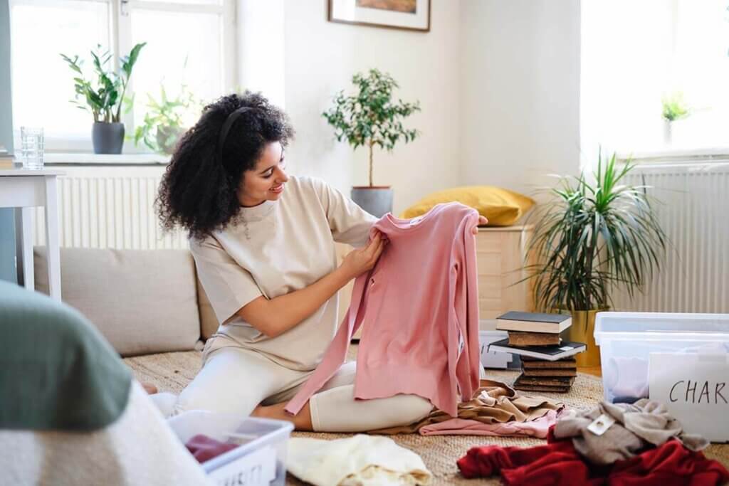Young woman sitting n floor holding up a pink sweater while packing.